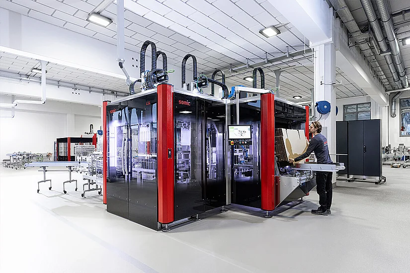 A person loading the carton magazine of a SOMIC 434 cartoning machine.